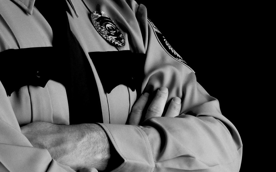 Gittings Protective Security uniform: light shirt, black tie, badge, and crossed arms